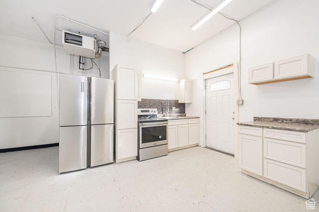 Kitchen featuring a sink, decorative backsplash, stainless steel appliances, and concrete flooring