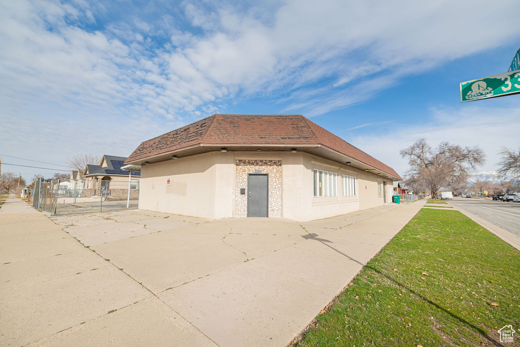 View of home's exterior featuring a shingled roof, mansard roof, a lawn, fence, and stucco siding