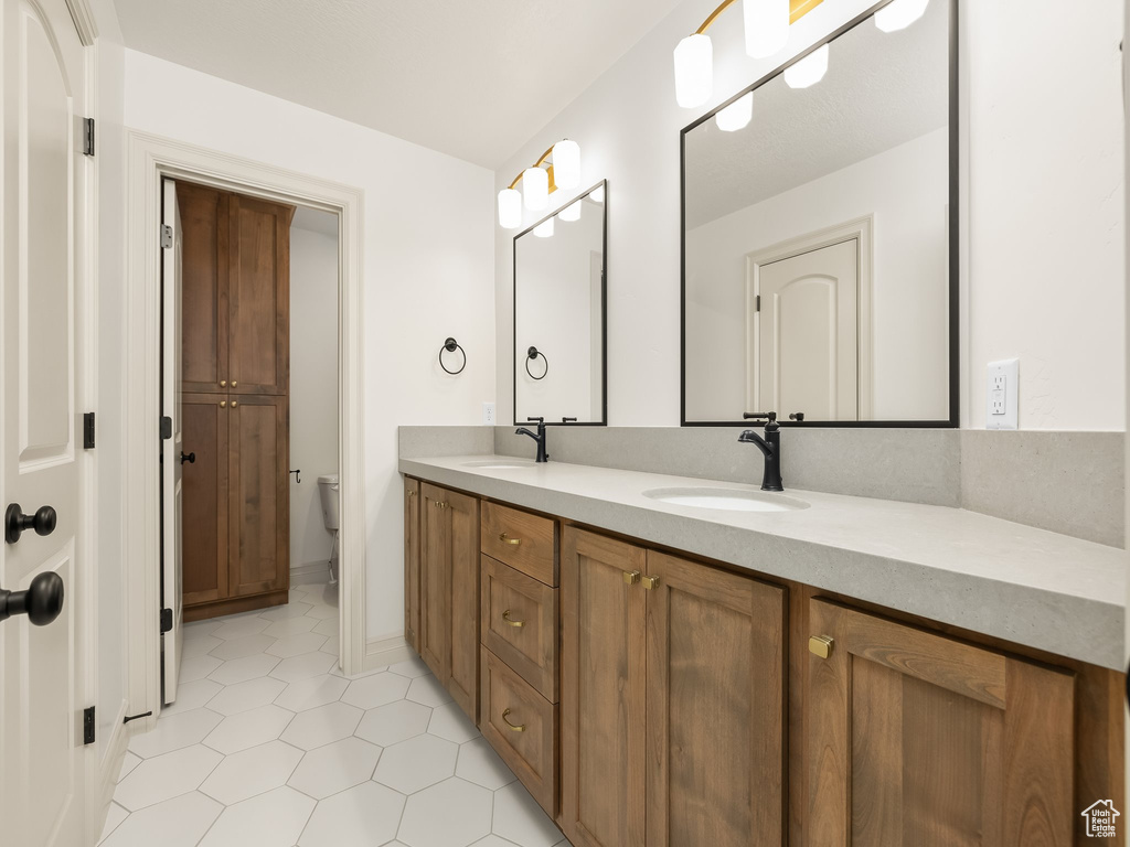 Bathroom with double vanity, a sink, toilet, and tile patterned floors