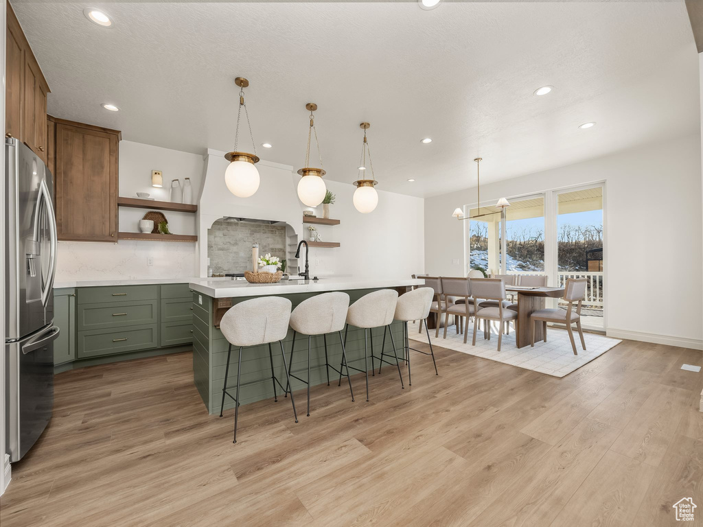 Kitchen with a breakfast bar, light countertops, light wood-type flooring, stainless steel fridge with ice dispenser, and open shelves