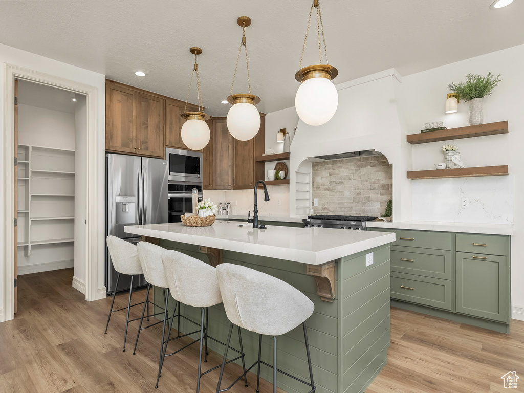 Kitchen featuring stainless steel appliances, open shelves, green cabinetry, and light wood-style flooring