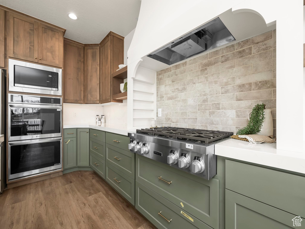 Kitchen featuring stainless steel appliances, ventilation hood, light countertops, and green cabinetry