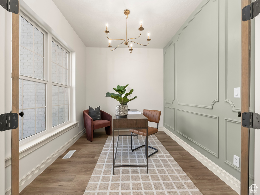 Home office featuring visible vents, a decorative wall, an inviting chandelier, wood finished floors, and baseboards