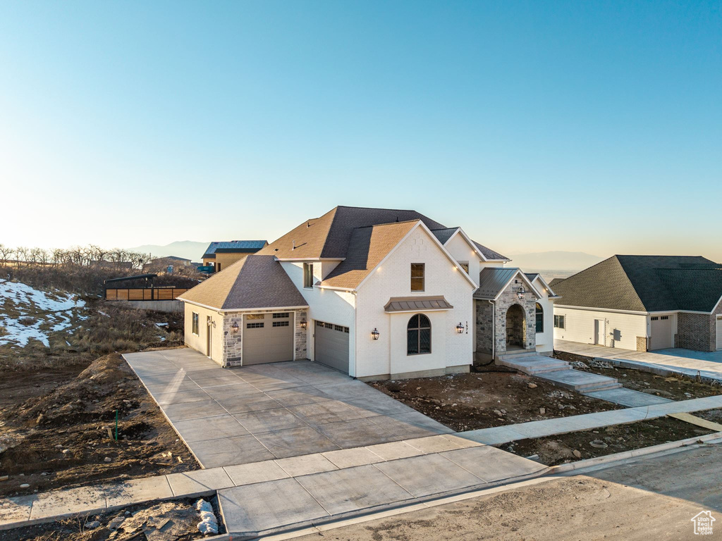 View of front of home featuring a garage, stone siding, roof with shingles, and driveway