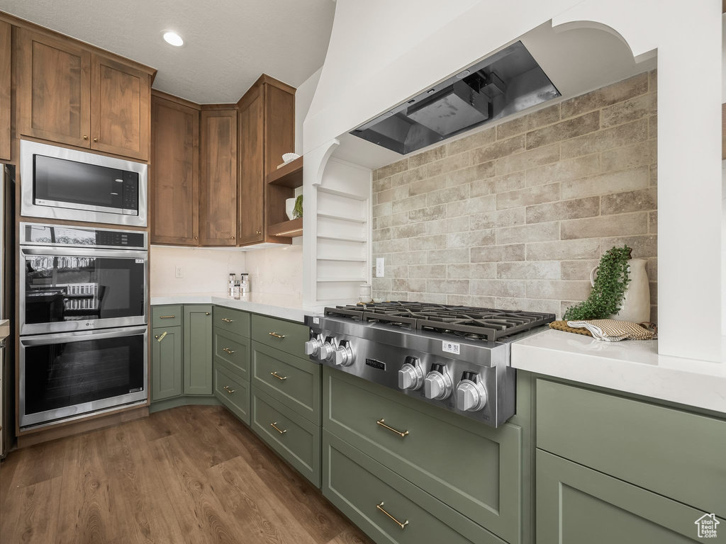 Kitchen featuring light countertops, green cabinets, appliances with stainless steel finishes, dark wood-type flooring, and wall chimney range hood