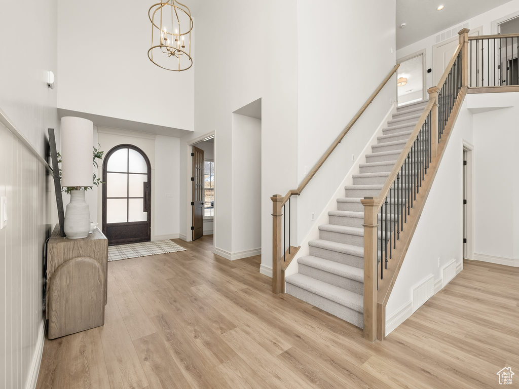 Foyer featuring stairs, an inviting chandelier, a towering ceiling, and light wood-style floors