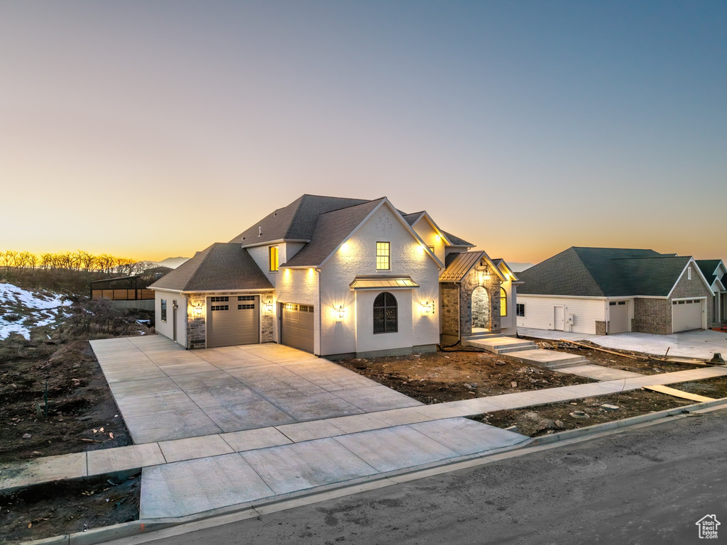 View of front of house featuring a garage, a shingled roof, concrete driveway, stone siding, and stucco siding