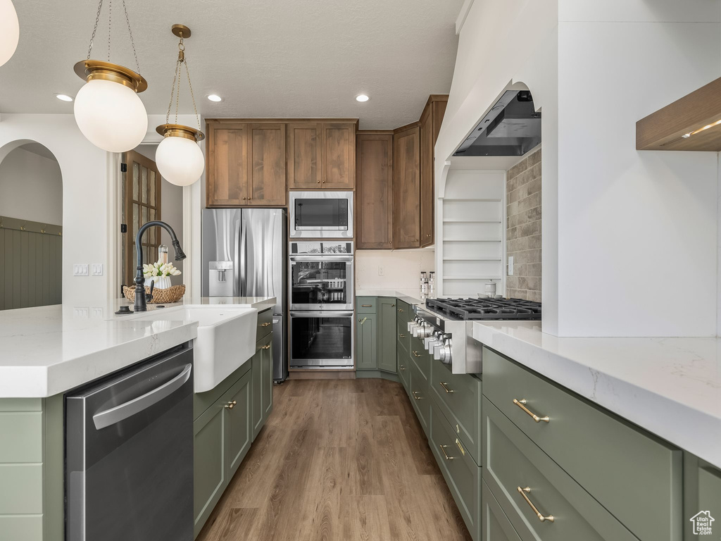 Kitchen with recessed lighting, green cabinets, appliances with stainless steel finishes, a sink, and wood finished floors