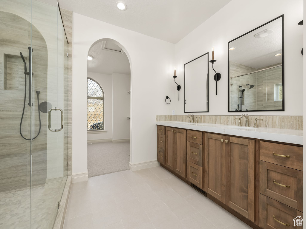 Bathroom featuring double vanity, a stall shower, a sink, and baseboards