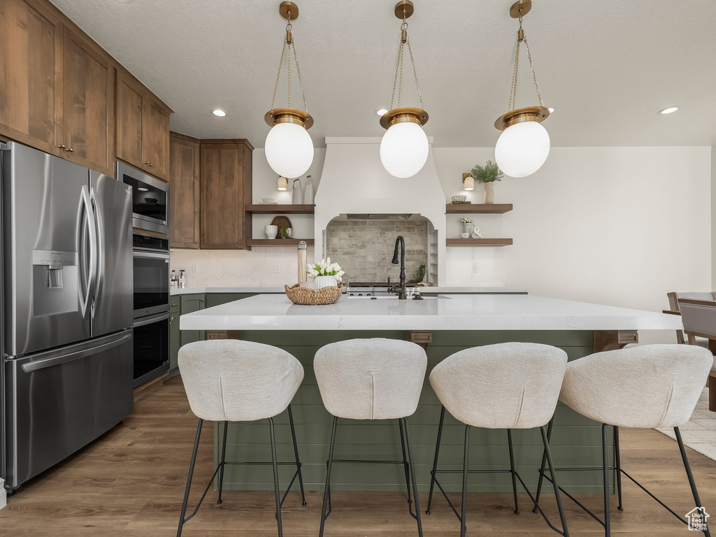 Kitchen featuring a sink, wood finished floors, light countertops, appliances with stainless steel finishes, and open shelves