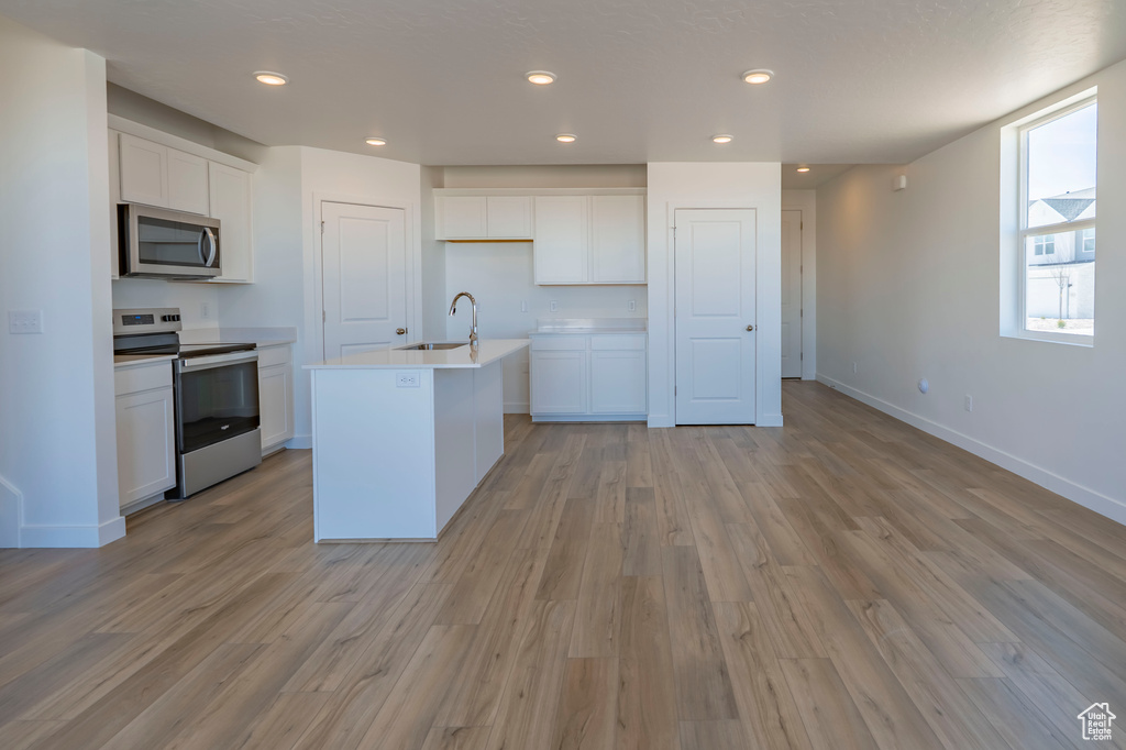 Kitchen with light wood finished floors, appliances with stainless steel finishes, white cabinetry, and a sink