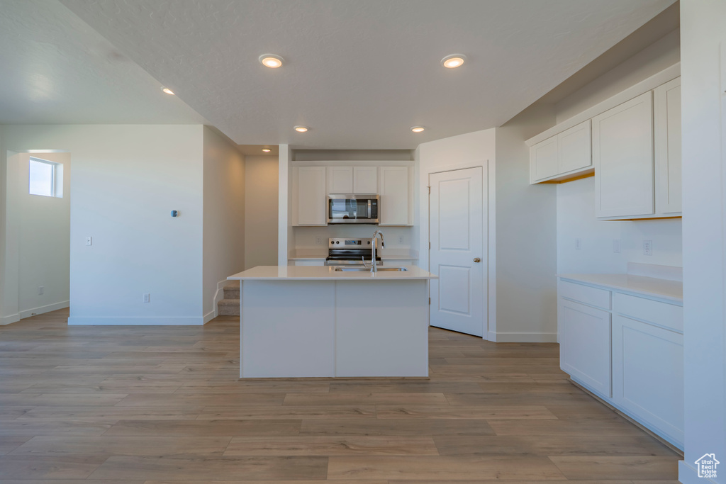 Kitchen featuring a sink, stainless steel appliances, light countertops, light wood-style floors, and white cabinetry