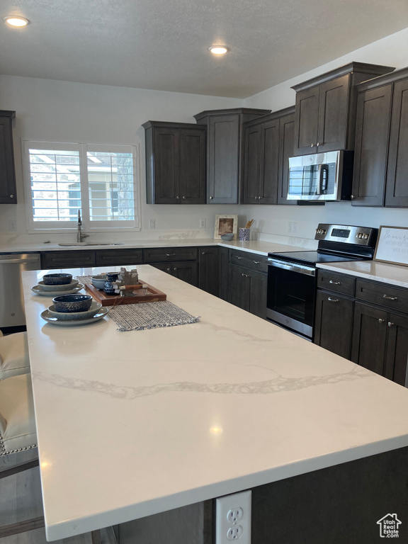 Kitchen featuring light stone counters, a center island, stainless steel appliances, recessed lighting, and a sink