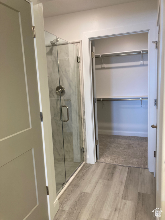 Bathroom featuring a stall shower, a walk in closet, and wood finished floors