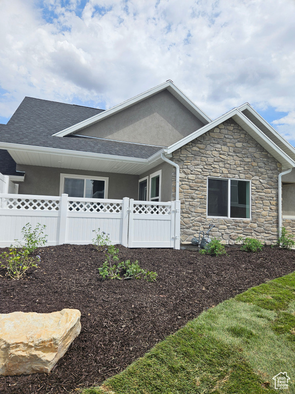 View of side of home featuring roof with shingles, fence, and stucco siding