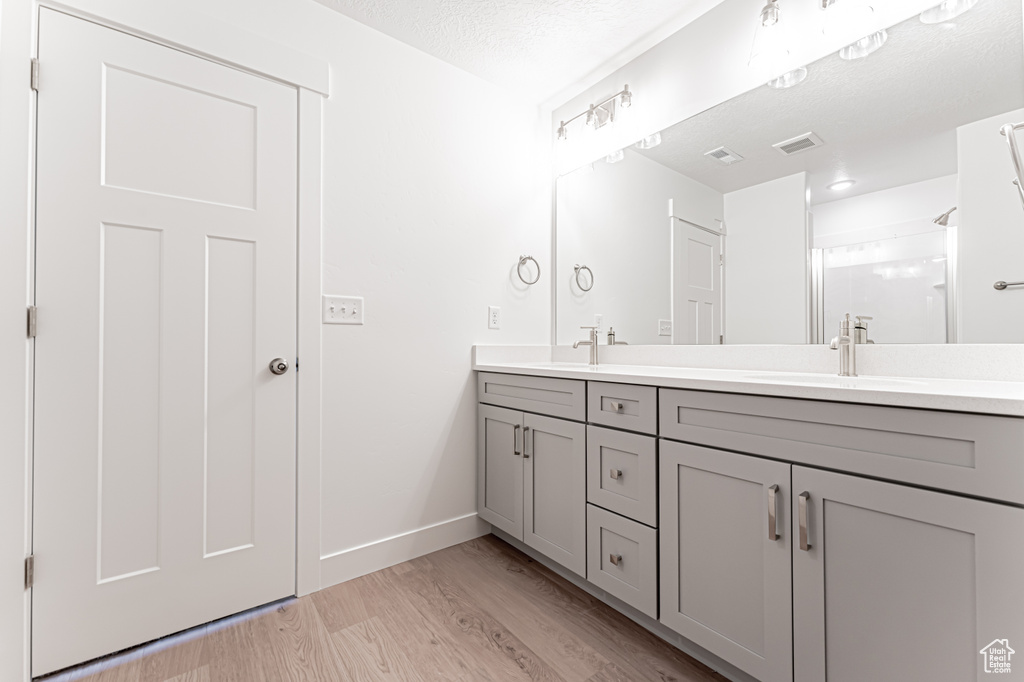 Bathroom with double vanity, wood finished floors, a textured ceiling, and a shower