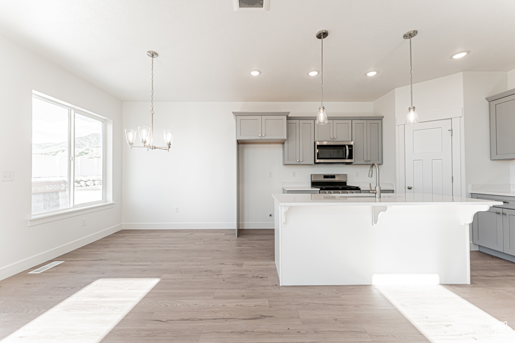 Kitchen with appliances with stainless steel finishes, gray cabinetry, light countertops, a kitchen bar, and recessed lighting