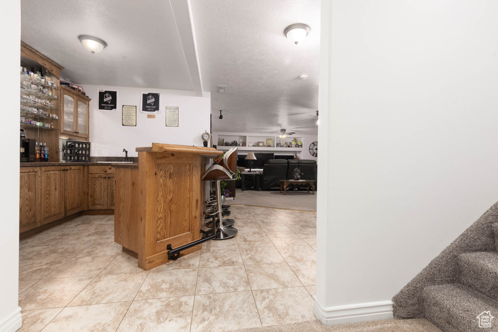 Kitchen featuring ceiling fan, a breakfast bar area, a peninsula, dark countertops, and glass insert cabinets