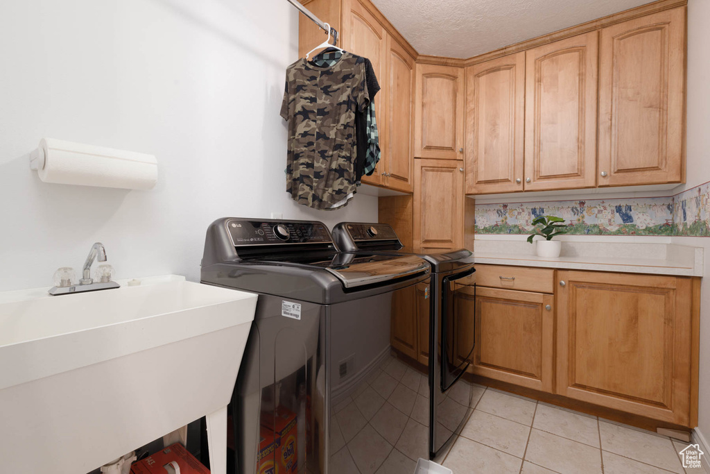 Clothes washing area featuring cabinet space, light tile patterned floors, washer and clothes dryer, a textured ceiling, and a sink