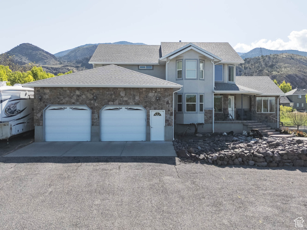View of front facade with driveway, a mountain view, a garage, stucco siding, and stone siding