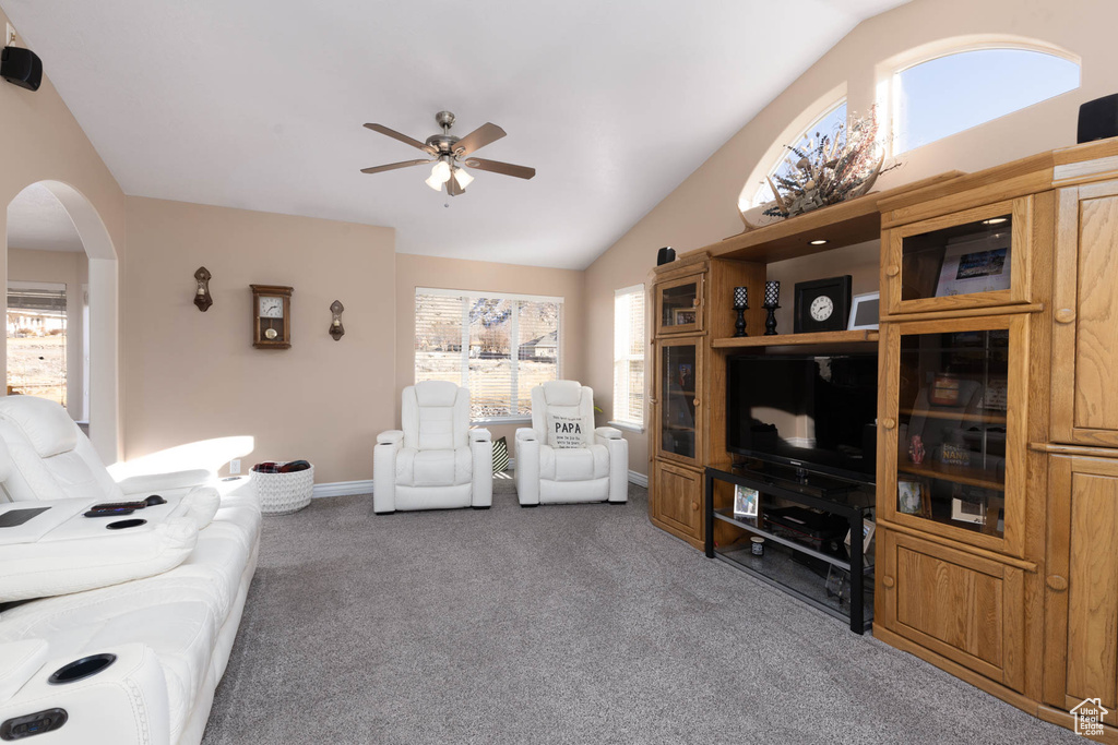 Carpeted living area with a wealth of natural light, lofted ceiling, arched walkways, and a ceiling fan