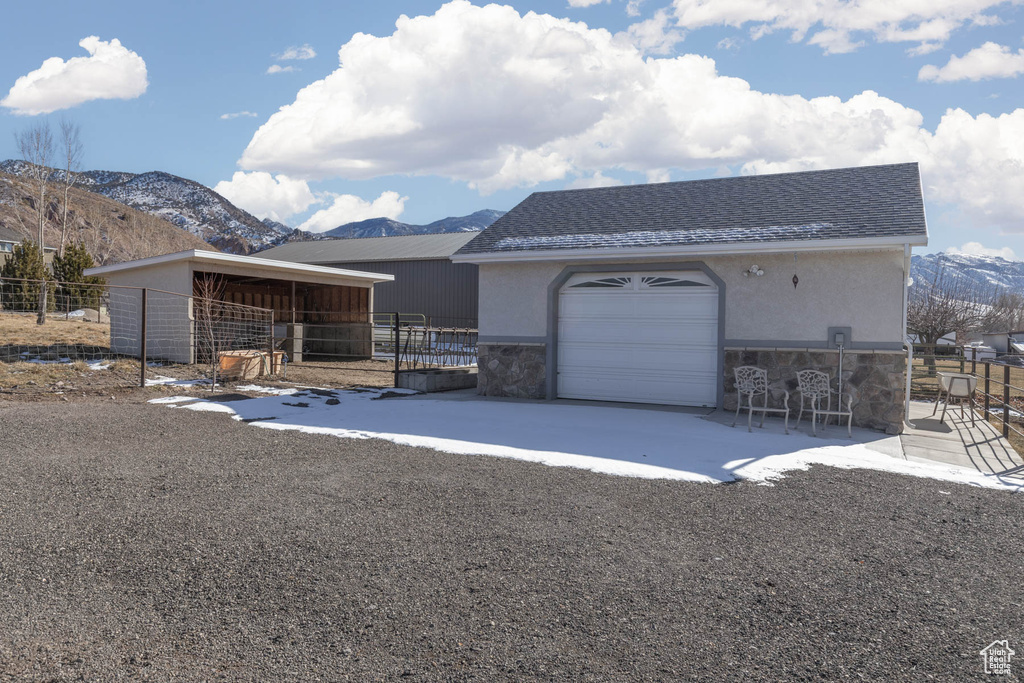 Single story home featuring a shingled roof, stone siding, an outbuilding, a mountain view, and stucco siding