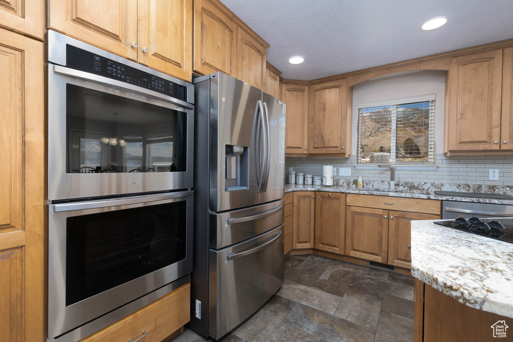 Kitchen featuring stainless steel appliances, tasteful backsplash, a sink, and light stone countertops