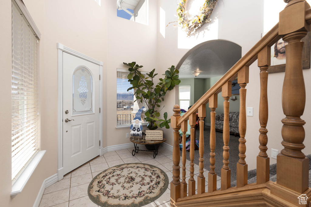 Entrance foyer featuring arched walkways, tile patterned floors, a towering ceiling, baseboards, and stairs