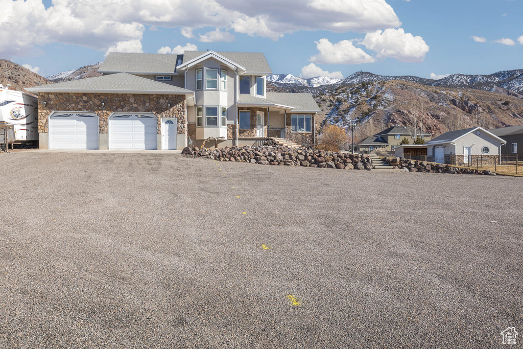 View of front facade with driveway, stone siding, an attached garage, and a mountain view