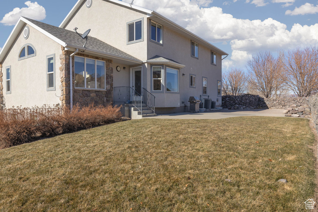 View of front facade with cooling unit, a shingled roof, stone siding, stucco siding, and a front lawn