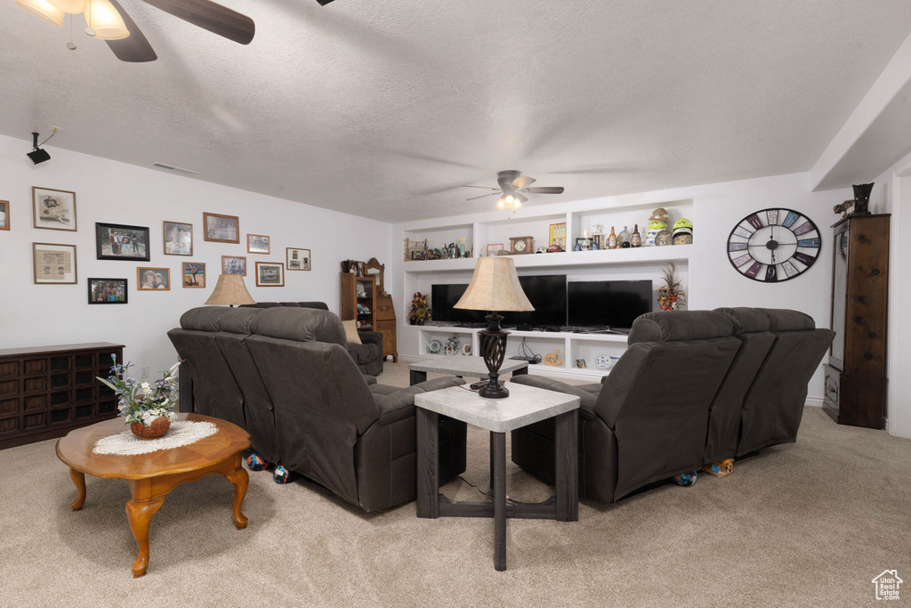 Living area with a textured ceiling, built in shelves, light carpet, a ceiling fan, and visible vents