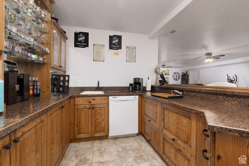 Kitchen with light tile patterned floors, brown cabinetry, a ceiling fan, dishwasher, and a sink