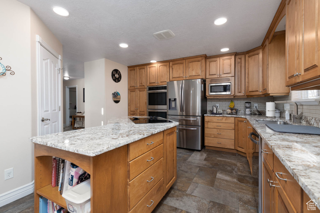 Kitchen featuring appliances with stainless steel finishes, brown cabinetry, decorative backsplash, and open shelves