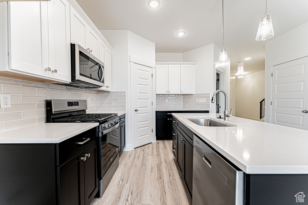 Kitchen featuring stainless steel appliances, dark cabinets, light wood-type flooring, white cabinetry, and light countertops