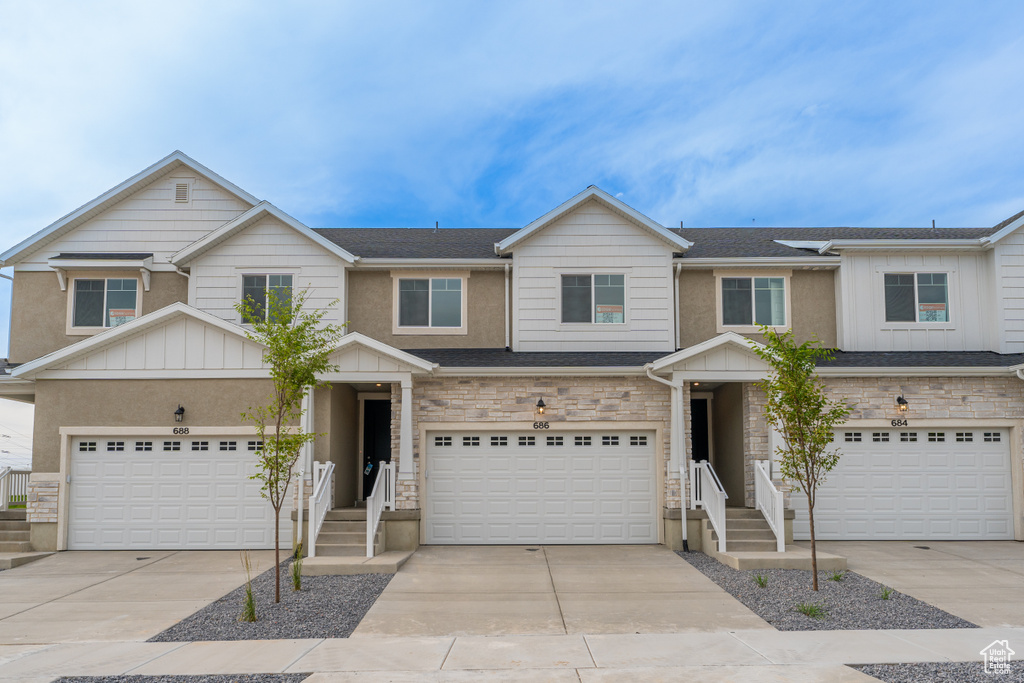 Townhome / multi-family property with concrete driveway, board and batten siding, an attached garage, and stone siding
