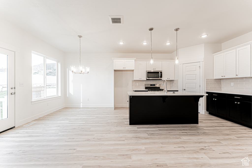 Kitchen with stainless steel appliances, decorative backsplash, white cabinetry, light countertops, and light wood-style floors