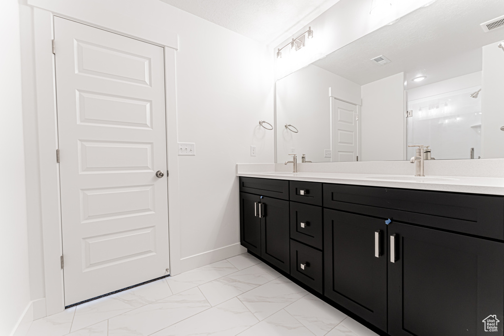 Bathroom with double vanity, marble look tile flooring, and a stall shower