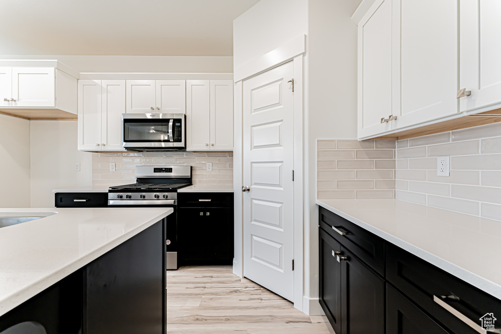 Kitchen with appliances with stainless steel finishes, dark cabinets, white cabinets, and light countertops