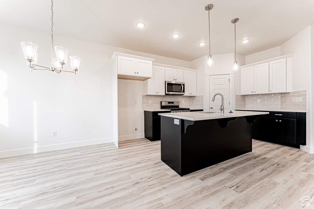 Kitchen with appliances with stainless steel finishes, a kitchen bar, light countertops, white cabinets, and tasteful backsplash