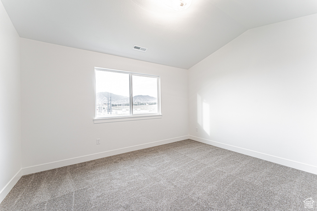 Carpeted empty room with lofted ceiling and baseboards