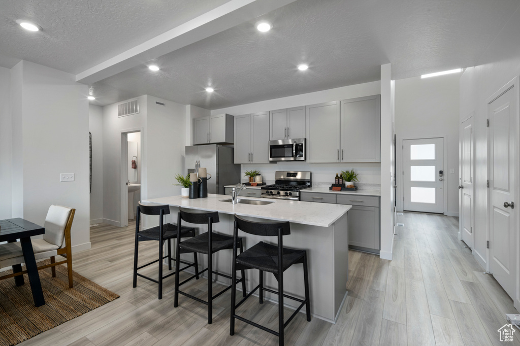 Kitchen featuring visible vents, gray cabinetry, appliances with stainless steel finishes, a sink, and a kitchen breakfast bar
