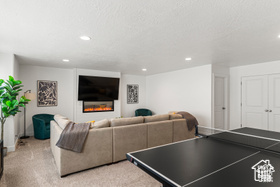 Rec room featuring light carpet, a textured ceiling, a glass covered fireplace, and recessed lighting