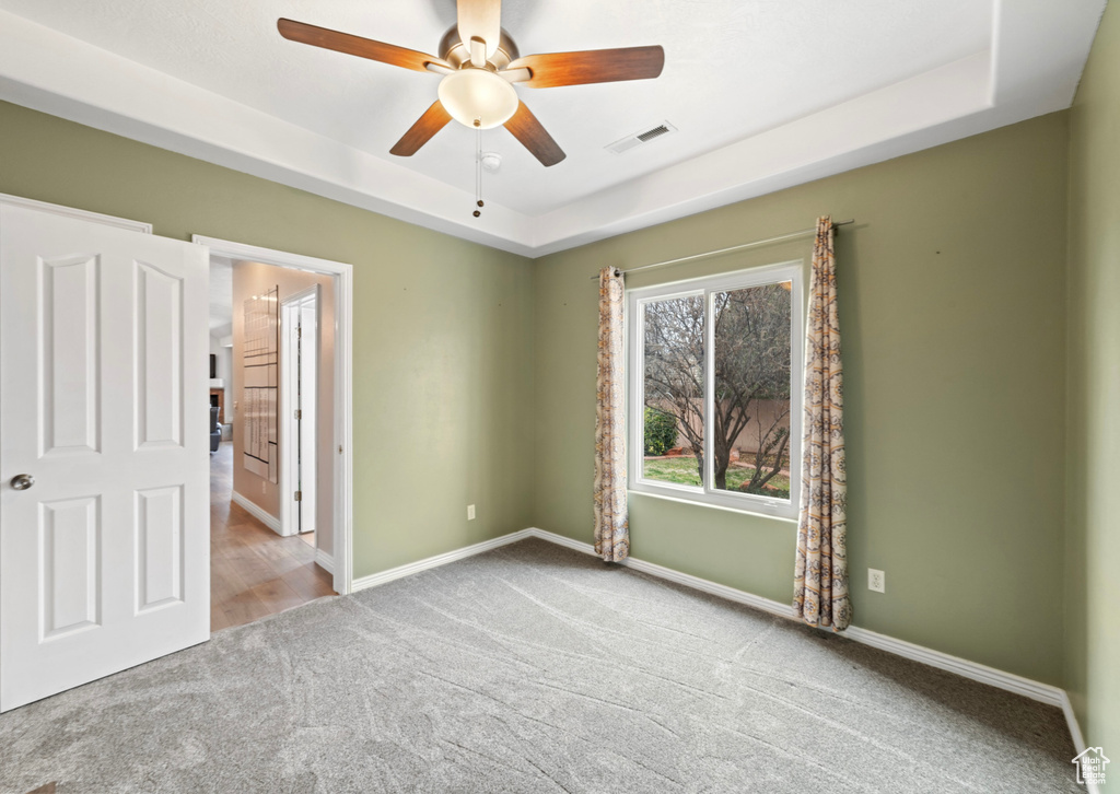 Unfurnished bedroom with carpet floors, a tray ceiling, baseboards, and a ceiling fan