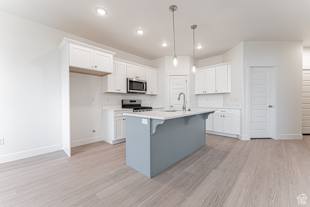 Kitchen with stainless steel appliances, light wood-style flooring, light countertops, white cabinetry, and a kitchen breakfast bar