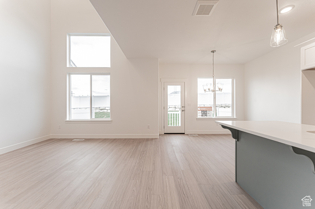 Unfurnished living room featuring a chandelier, healthy amount of natural light, and light wood-type flooring