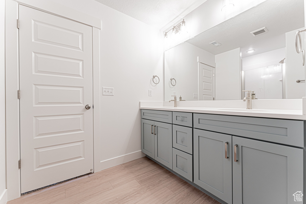 Bathroom with double vanity, wood finished floors, and a shower