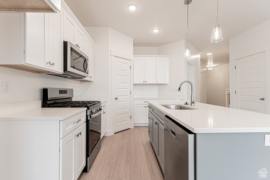 Kitchen featuring appliances with stainless steel finishes, light wood finished floors, recessed lighting, an island with sink, and white cabinets