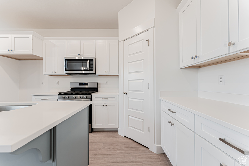 Kitchen featuring appliances with stainless steel finishes, light countertops, white cabinets, and light wood-style flooring