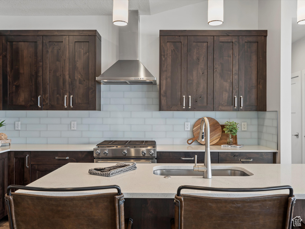 Kitchen featuring wall chimney exhaust hood, dark brown cabinets, a sink, and gas stove