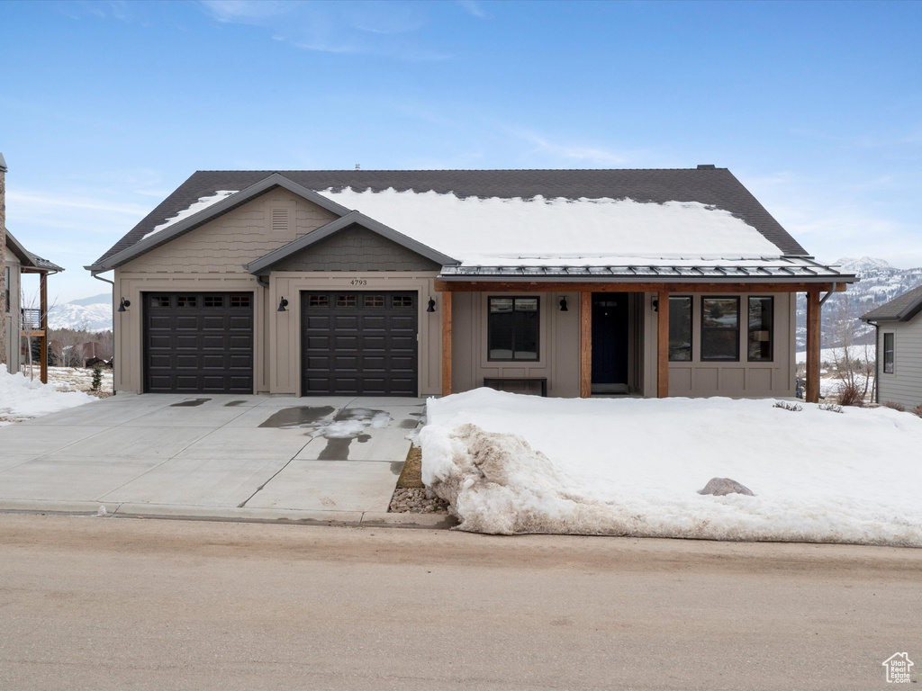 View of front of home with an attached garage, board and batten siding, a standing seam roof, metal roof, and driveway